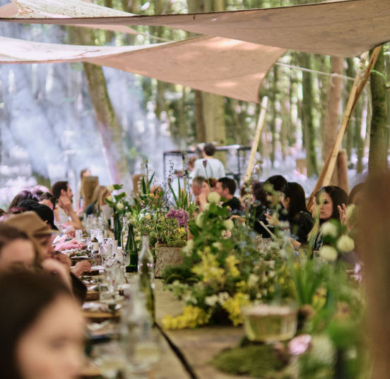 A large group of people seated at Nomadic's communal dining wood-crafted table